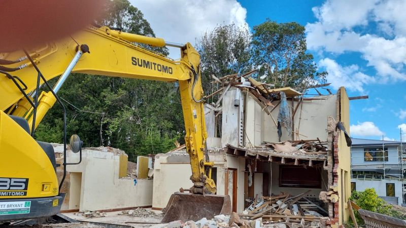 House demolition in progress: Sumitomo excavator pulling down rendered brick residential home