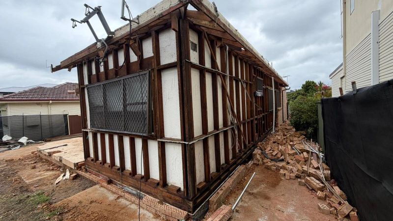 Side view of a house stripped back to its timber frame on a brick base after cladding removal