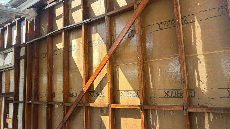 External wall showing removed fibro sheeting, exposed timber studs and internal plasterboard lining