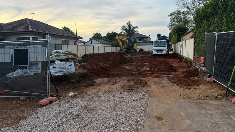 Cleared residential block with gravel driveway, excavator and tipper truck ready for new construction