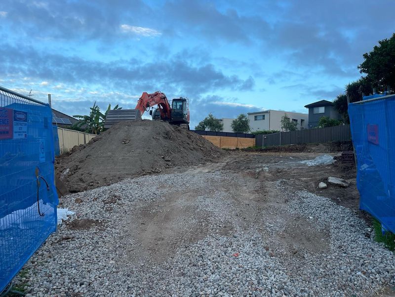 Excavator working on a soil stockpile beside a graded residential site