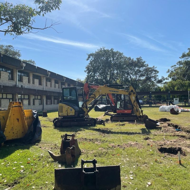 Yellow Yanmar excavator and attachments on a grassed residential block