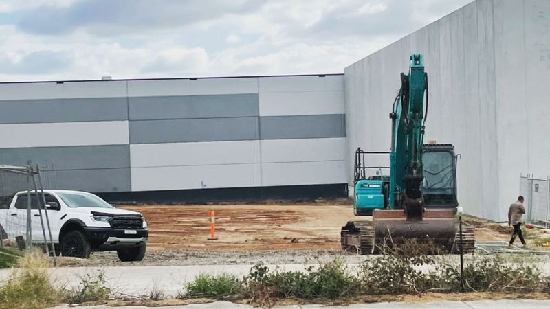 Kobelco excavator on a cleared commercial slab beside a new warehouse in Sydney's west