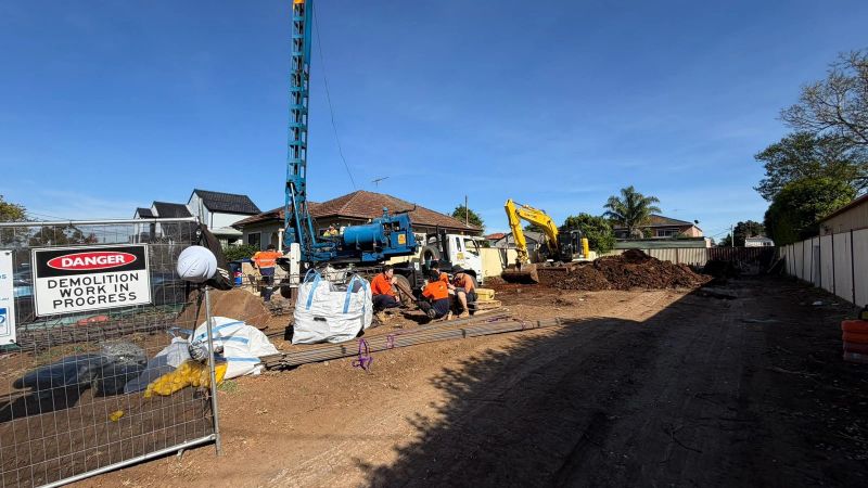 Demolition site safety signage and fencing with piling rig and excavator equipment visible